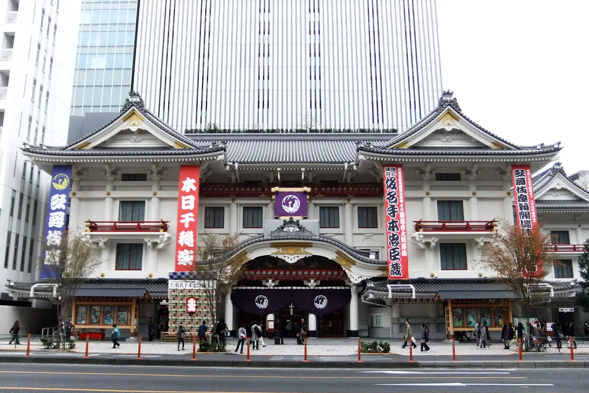 Ginza'daki Kabuki-za tiyatrosunun beyaz ve kırmızı cephesi; arkasında yükselen yüksek bir ofis kulesi ve kaldırım boyunca yürüyen yayalar